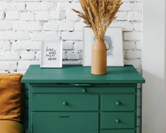 Room with a green dresser, vase, and framed art